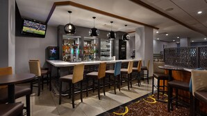A bar area with multiple seating options, a television mounted on the wall, and a variety of bottles and glasses on shelves. - Hilton Garden Inn Montréal Centre-ville (Montreal)
