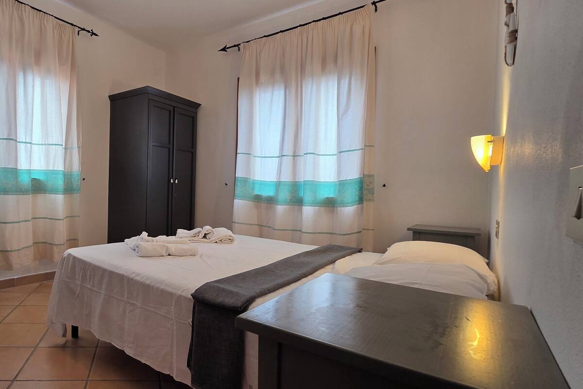 Une chambre d’hôtel comprenant un lit, une table de chevet, une armoire et des rideaux à rayures turquoise.