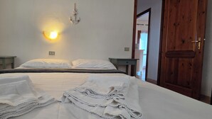 A neatly made bed with white linens and towels, a wall-mounted light fixture, and a wooden door. - RESIDENCE LU LAMONI COSTA NORD (Aglientu)