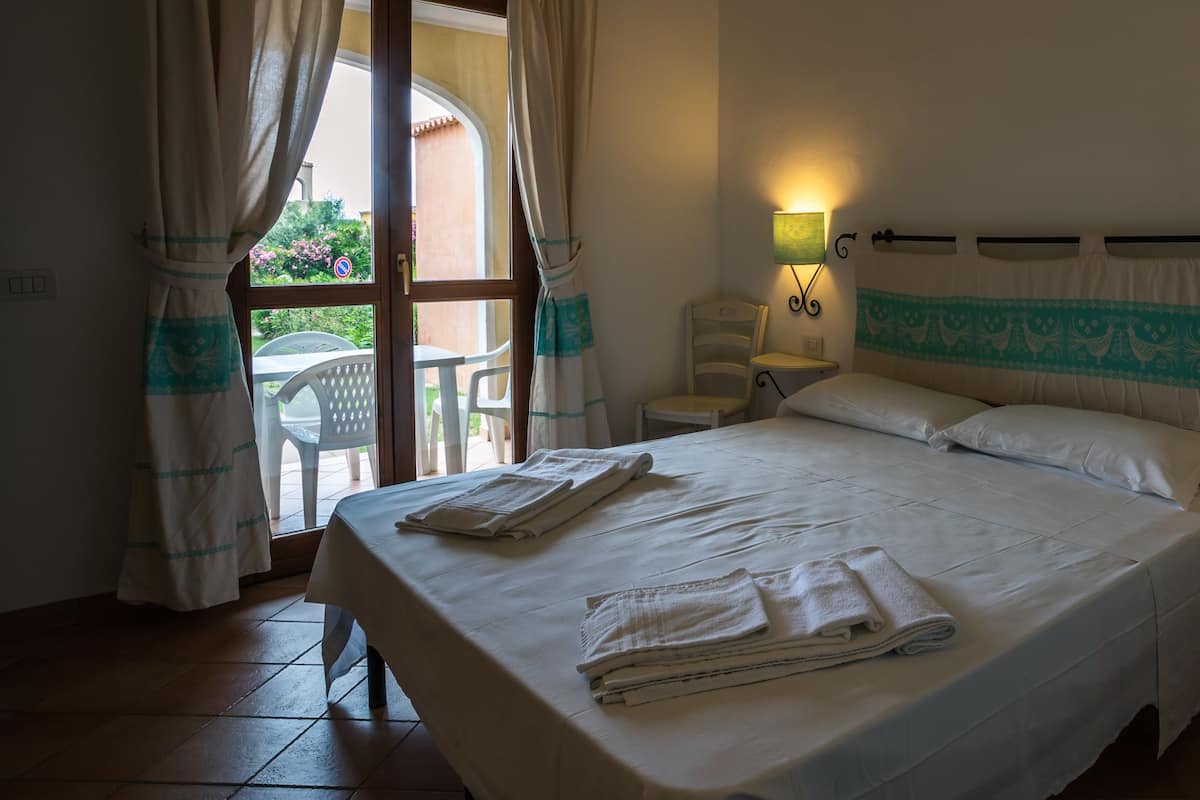 Une chambre d’hôtel avec un lit, une table de chevet, une lampe et une vue sur l’extérieur par une fenêtre.