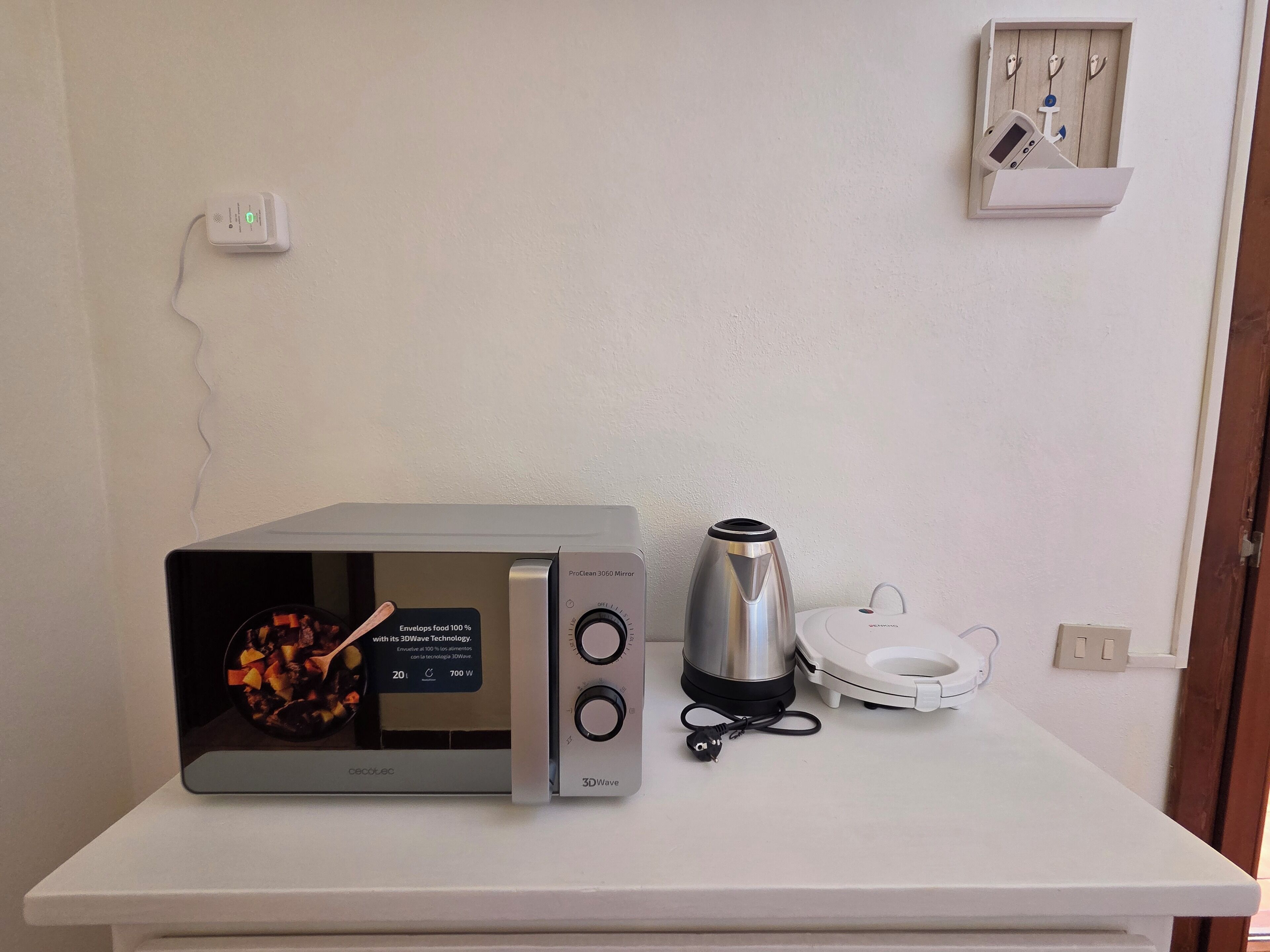 A microwave with a 3DWave technology label, a stainless steel electric kettle, and a white electric rice cooker on a white countertop.