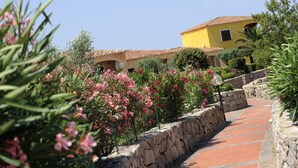 A stone pathway leading to a yellow building with a tiled roof. - RESIDENCE LU LAMONI COSTA NORD (Aglientu)
