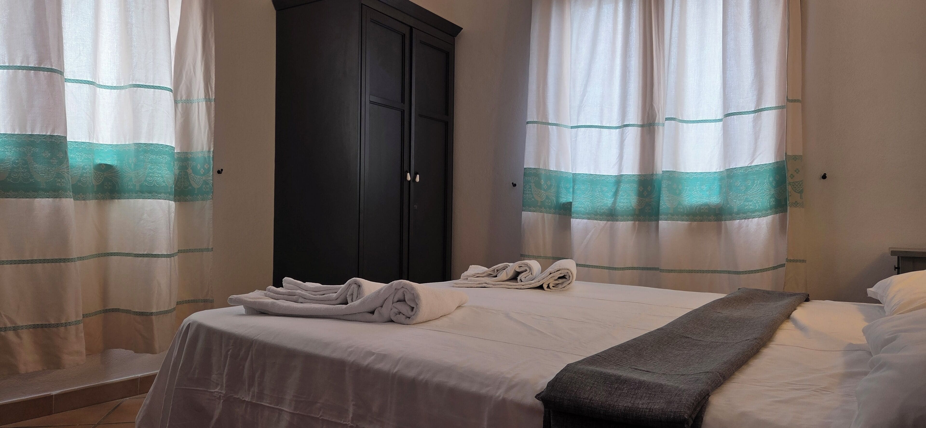 Une chambre d’hôtel avec un lit, une armoire sombre et des rideaux à motifs turquoise.