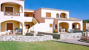 A multi-story building with balconies, outdoor seating, and a stone retaining wall. - RESIDENCE LU LAMONI COSTA NORD (Aglientu)