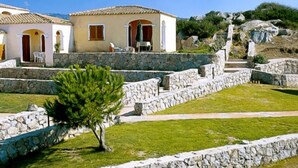 A traditional stone-walled building with a tiled roof, a small patio area with outdoor seating, and a staircase leading to an upper level. - RESIDENCE LU LAMONI COSTA NORD (Aglientu)