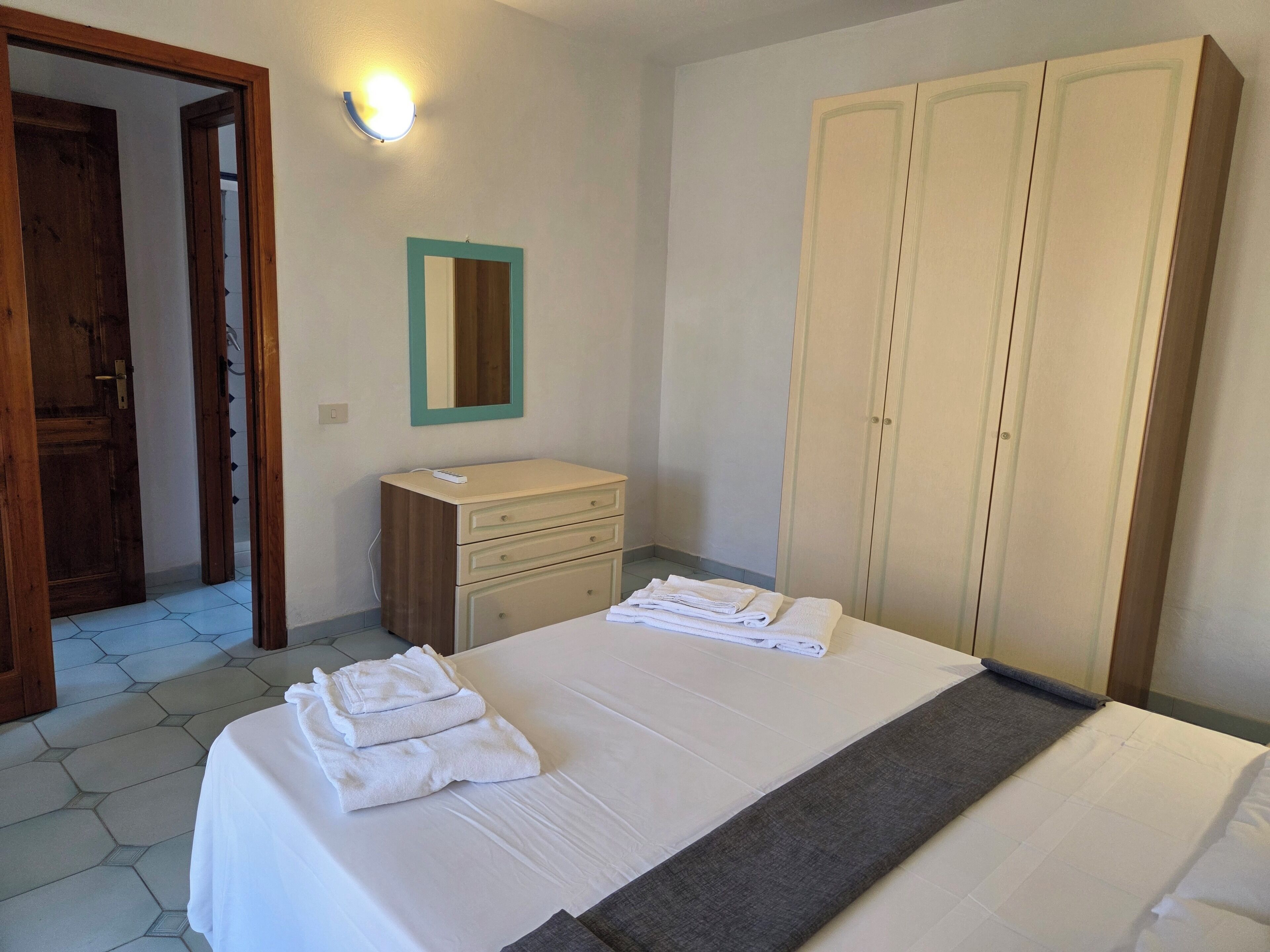 A bedroom with a bed, a dresser, a wardrobe, and a mirror.