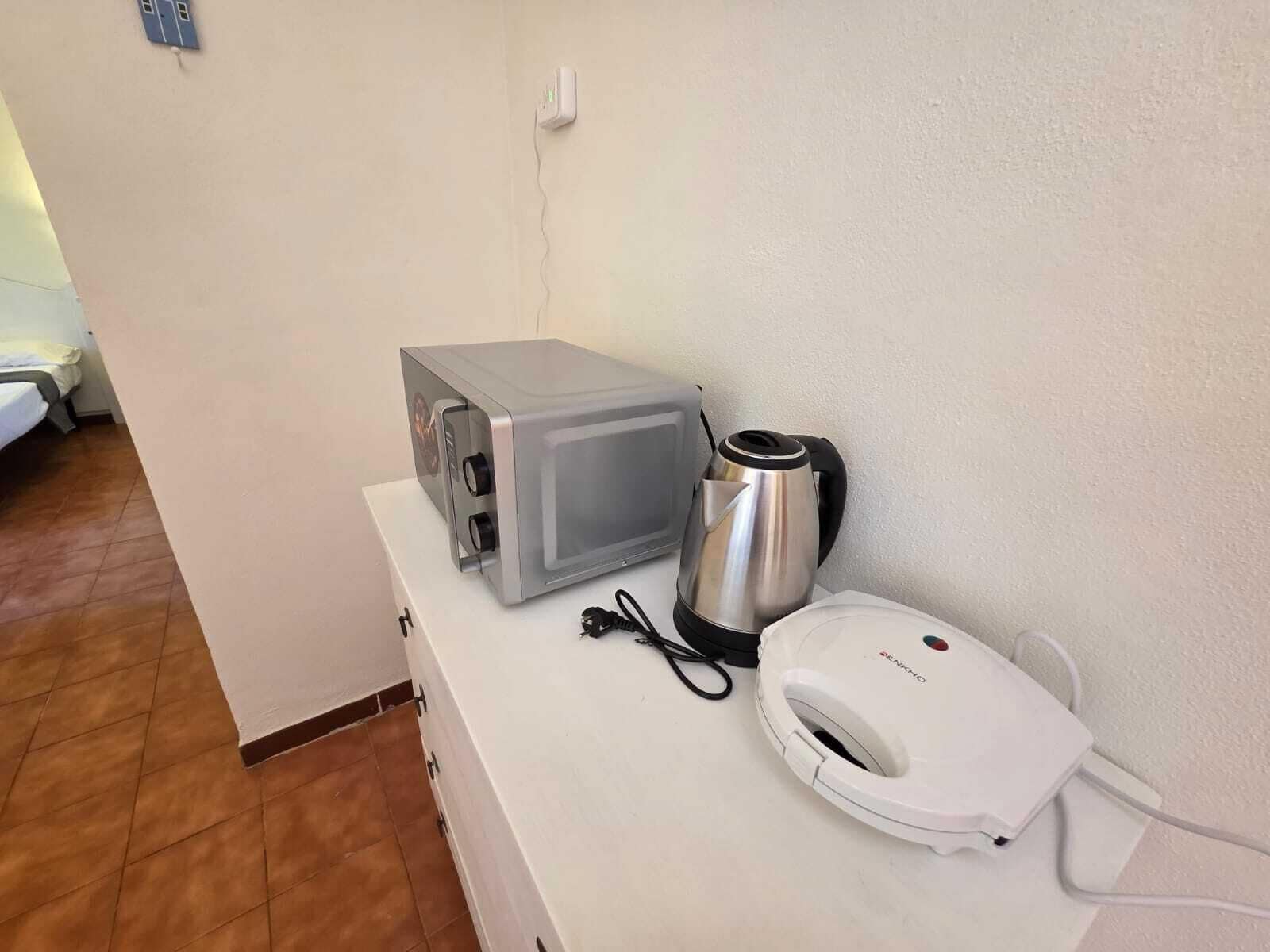 Eine Küchenzeile mit Mikrowelle, Wasserkocher und Kaffeemaschine auf einer weißen Arbeitsplatte.