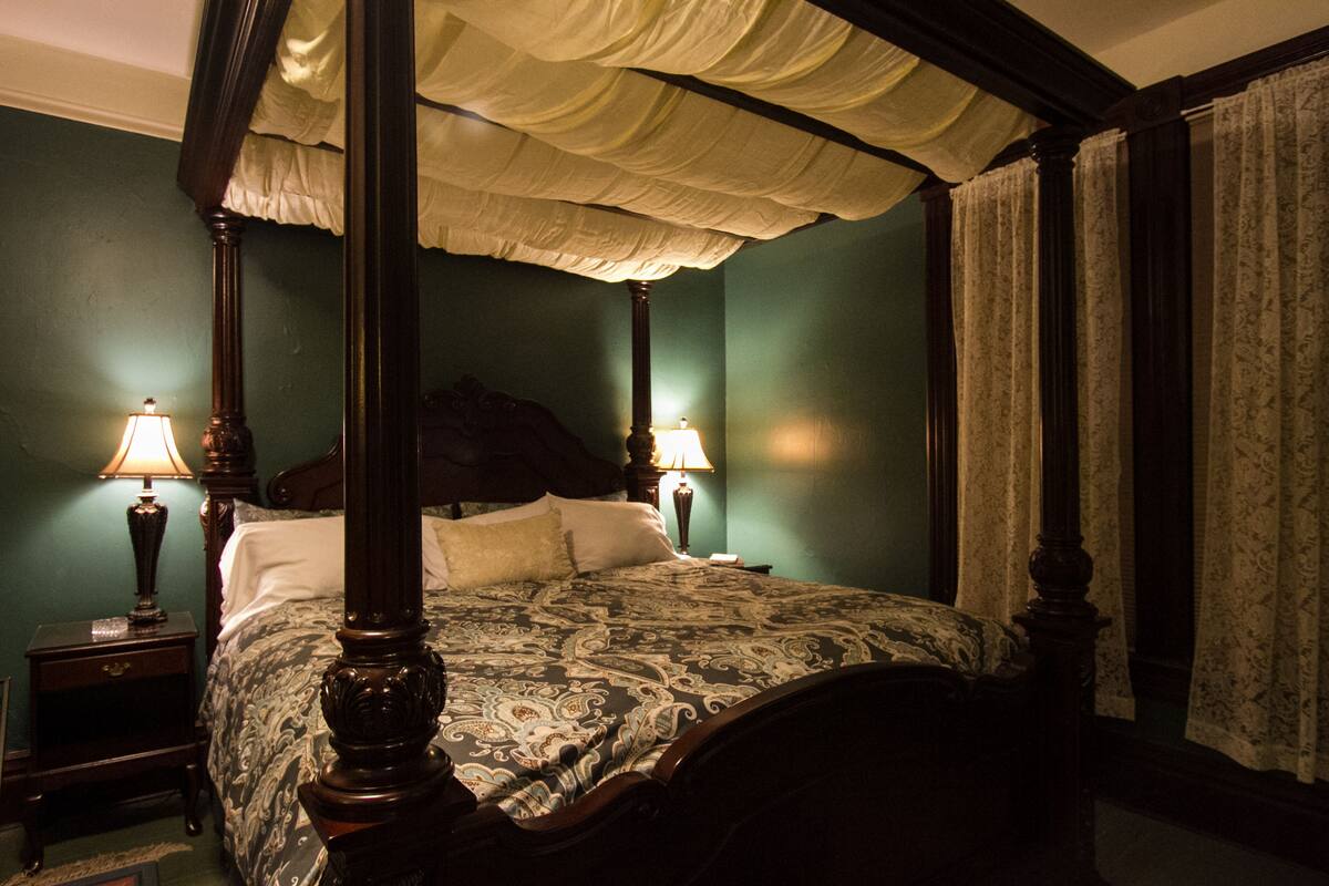 A four-poster bed with a canopy, two bedside tables with lamps, and a green wall.