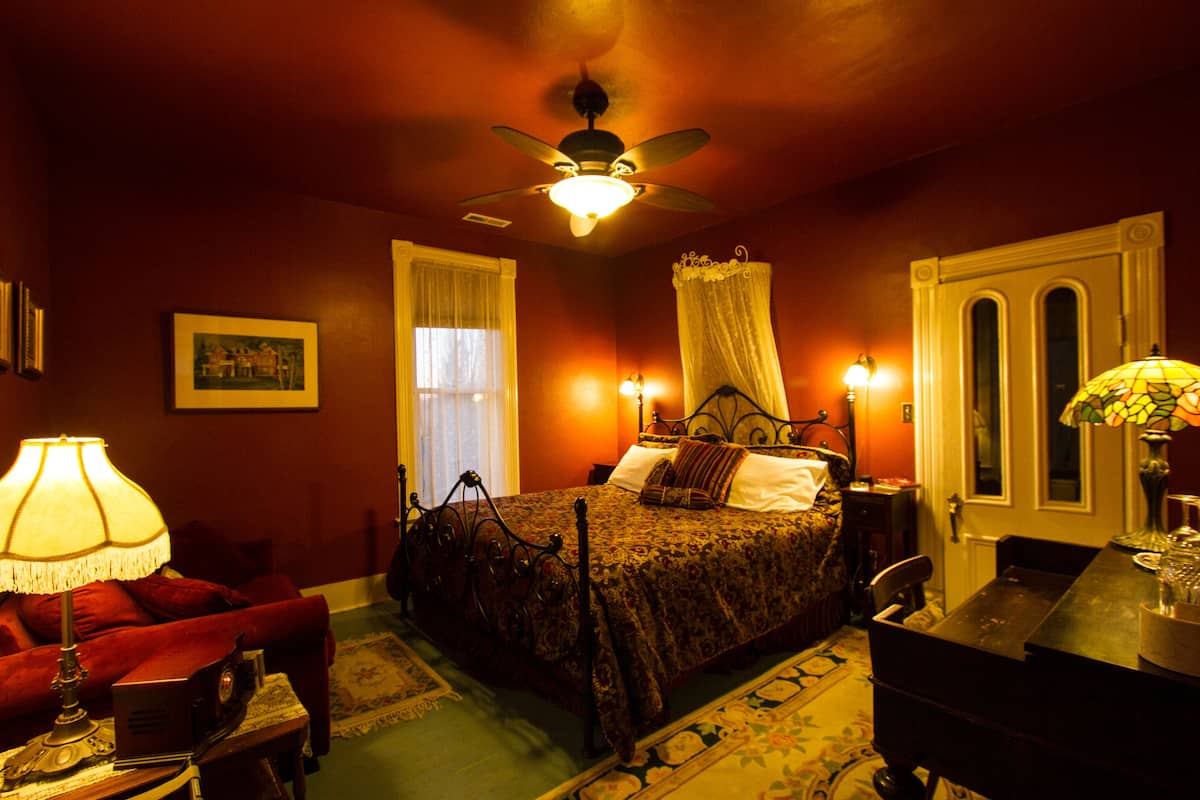 A bedroom with a four-poster bed, a ceiling fan, a nightstand, a desk, and a chair.