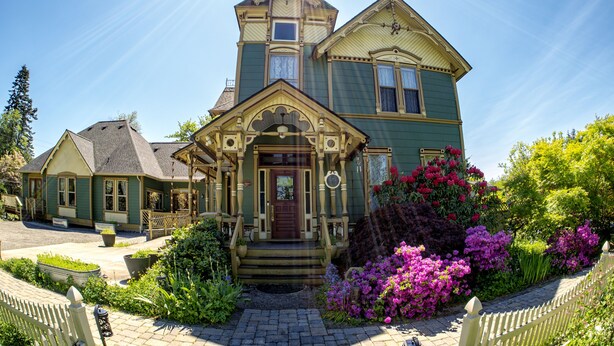 Et victoriansk hus med en markant veranda, et tårn og en velplejet have med mange blomster.