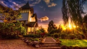 Et traditionelt hus med saddeltag, omgivet af en velholdt have og en sti, der fører til indgangen.