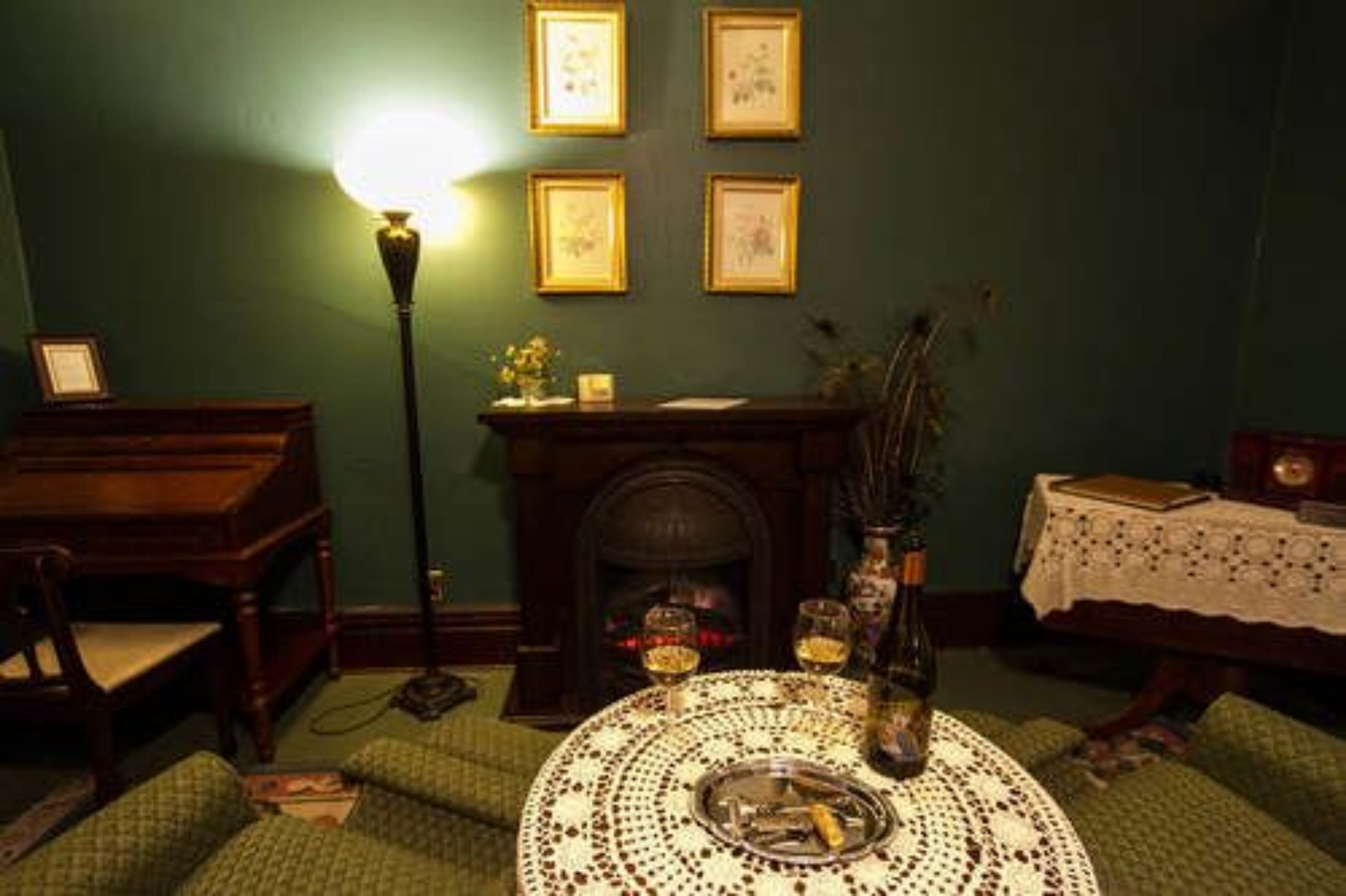 Una habitación con chimenea, una mesa con un adorno decorativo, una lámpara y cuadros en la pared.