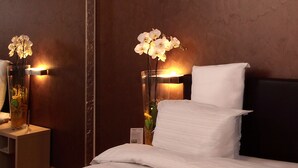 A neatly made bed with two white bathrobes, a bedside table with a vase of flowers, and a wall-mounted lamp. - Euro Hotel Residence (Concorezzo)