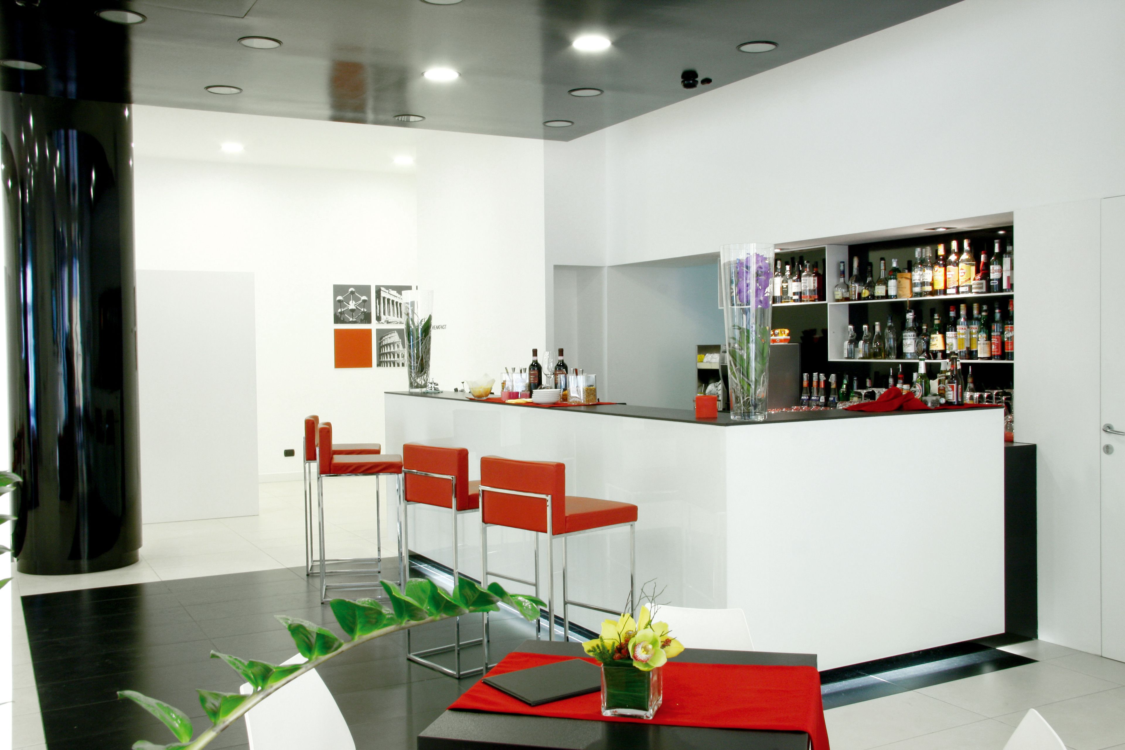 Zona bar moderna con un bancone bianco, sgabelli rossi e una selezione di bottiglie di liquore.
