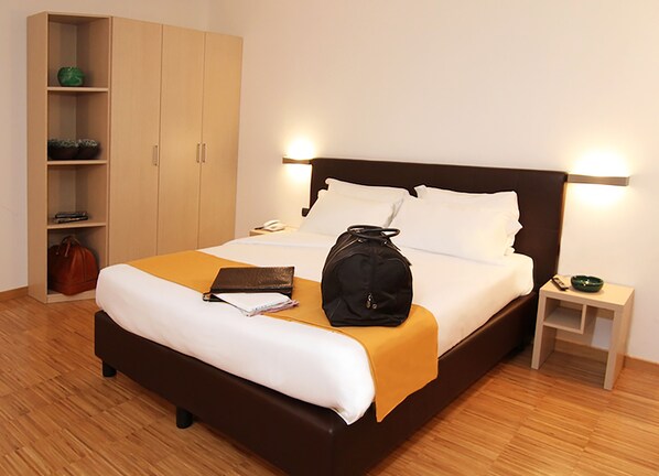 A hotel room with a bed, a wardrobe, a bedside table with a lamp, and a nightstand.