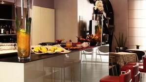A modern bar area with a long counter, white bar stools, and a variety of food and drink items displayed. - Euro Hotel Residence (Concorezzo)