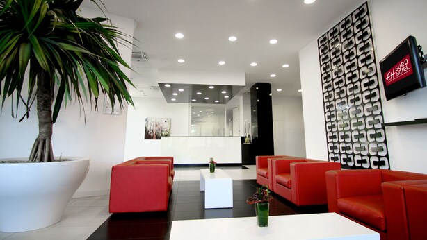 A modern hotel lobby with red seating, a large potted plant, and a reception desk. - Euro Hotel Residence (Concorezzo)