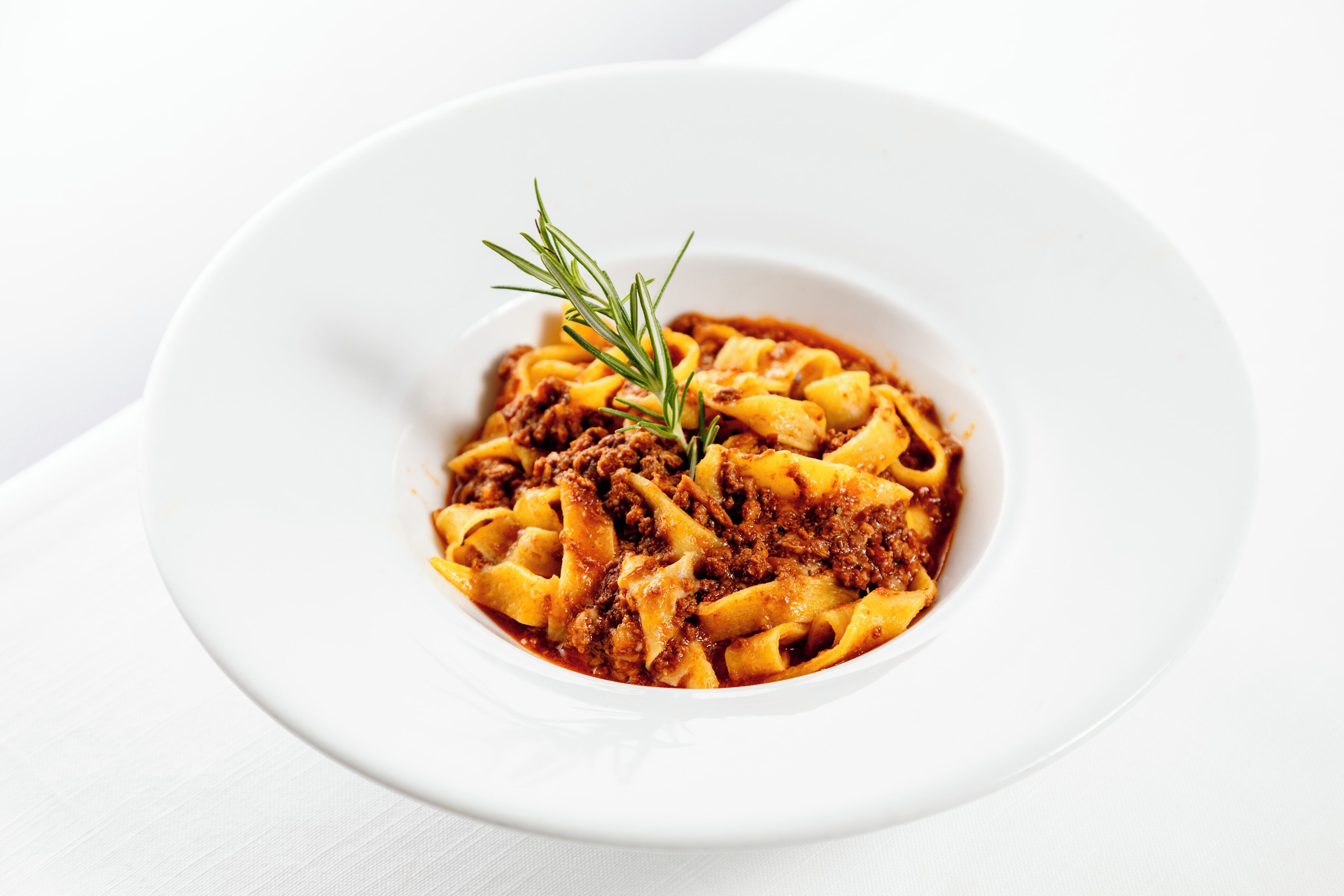 A white plate with pasta and a sprig of rosemary.