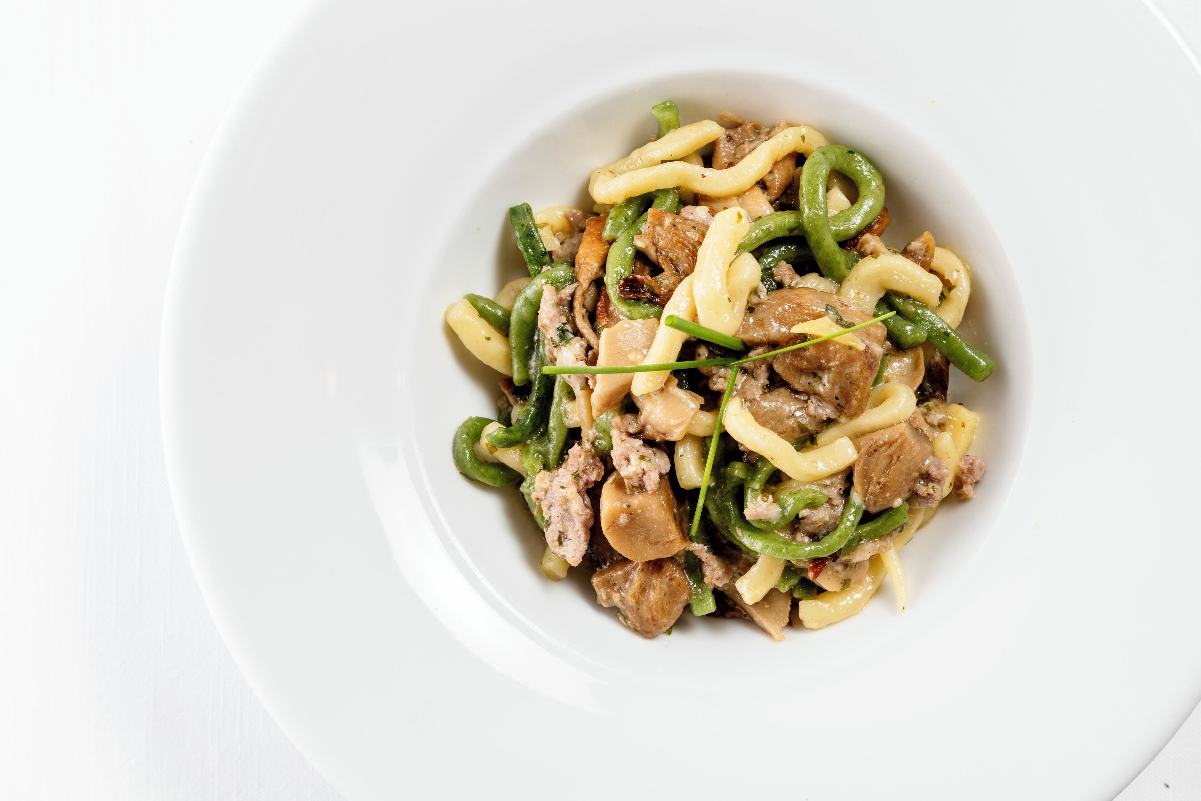 A white plate with a stir-fry dish containing meat, green beans, and noodles.