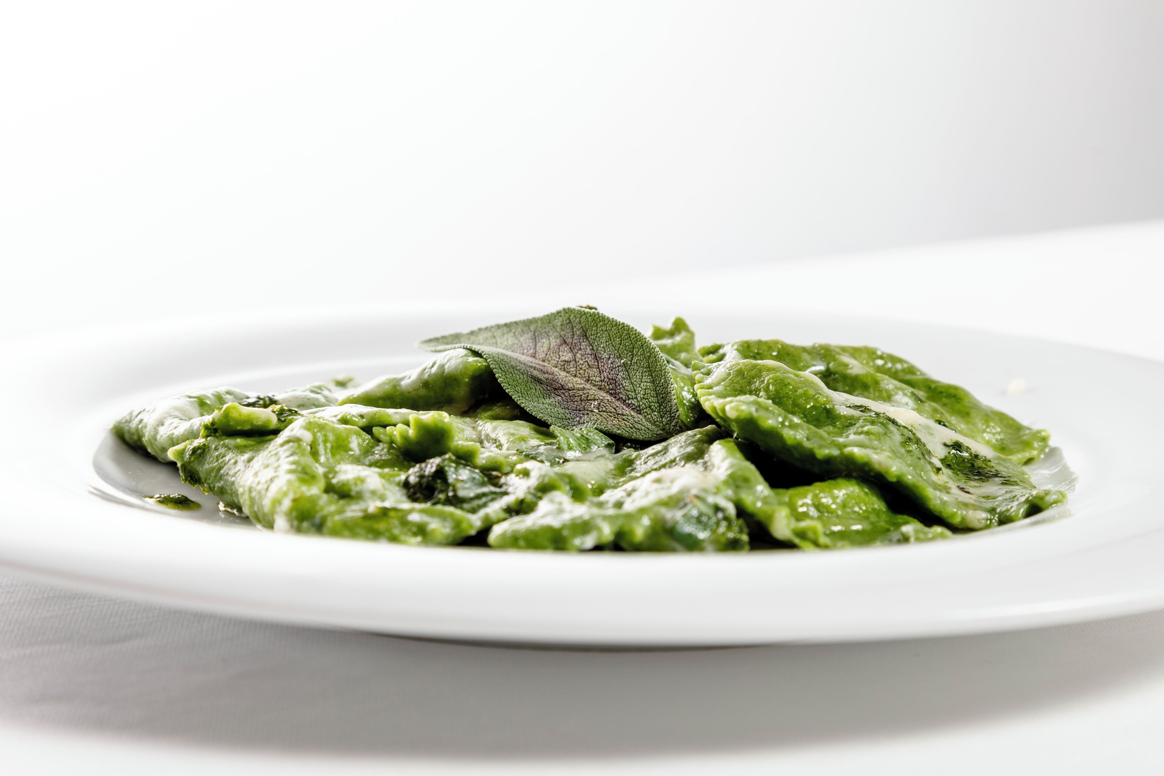 Un plato de pasta verde con una decoración de hoja sobre un plato blanco.
