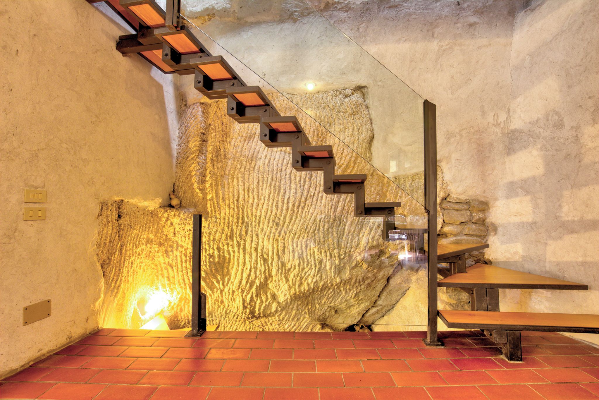 A staircase with wooden steps leading to a higher level, a stone wall with a textured surface, and a brick floor.