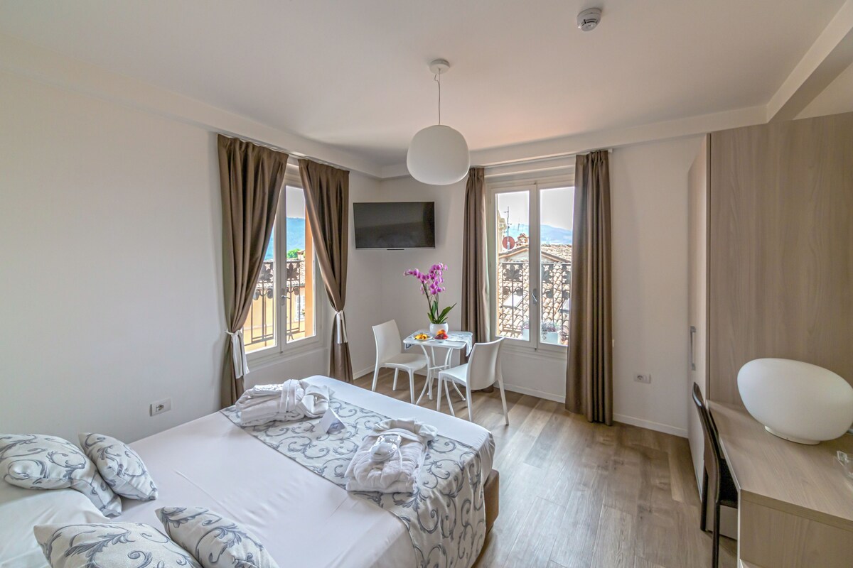 Habitación de hotel con cama, escritorio, silla, televisor y balcón con vistas.