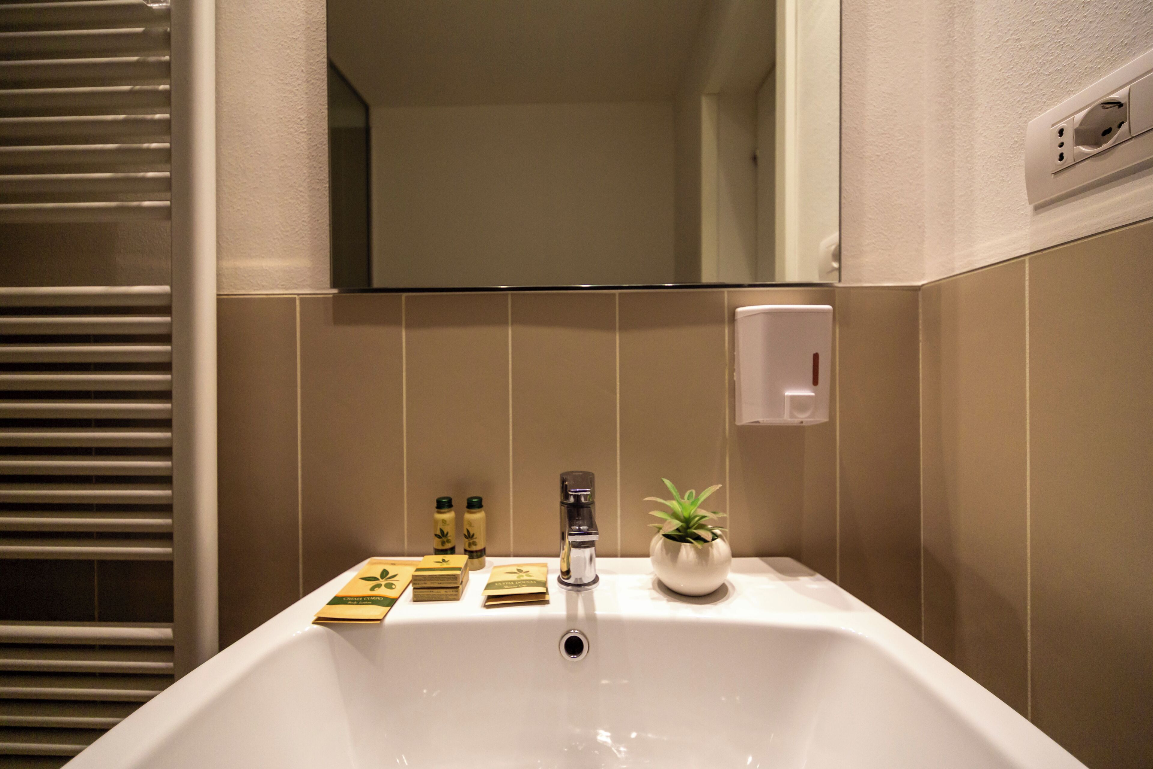 Un baño con lavamanos blanco, un espejo y una planta en maceta.