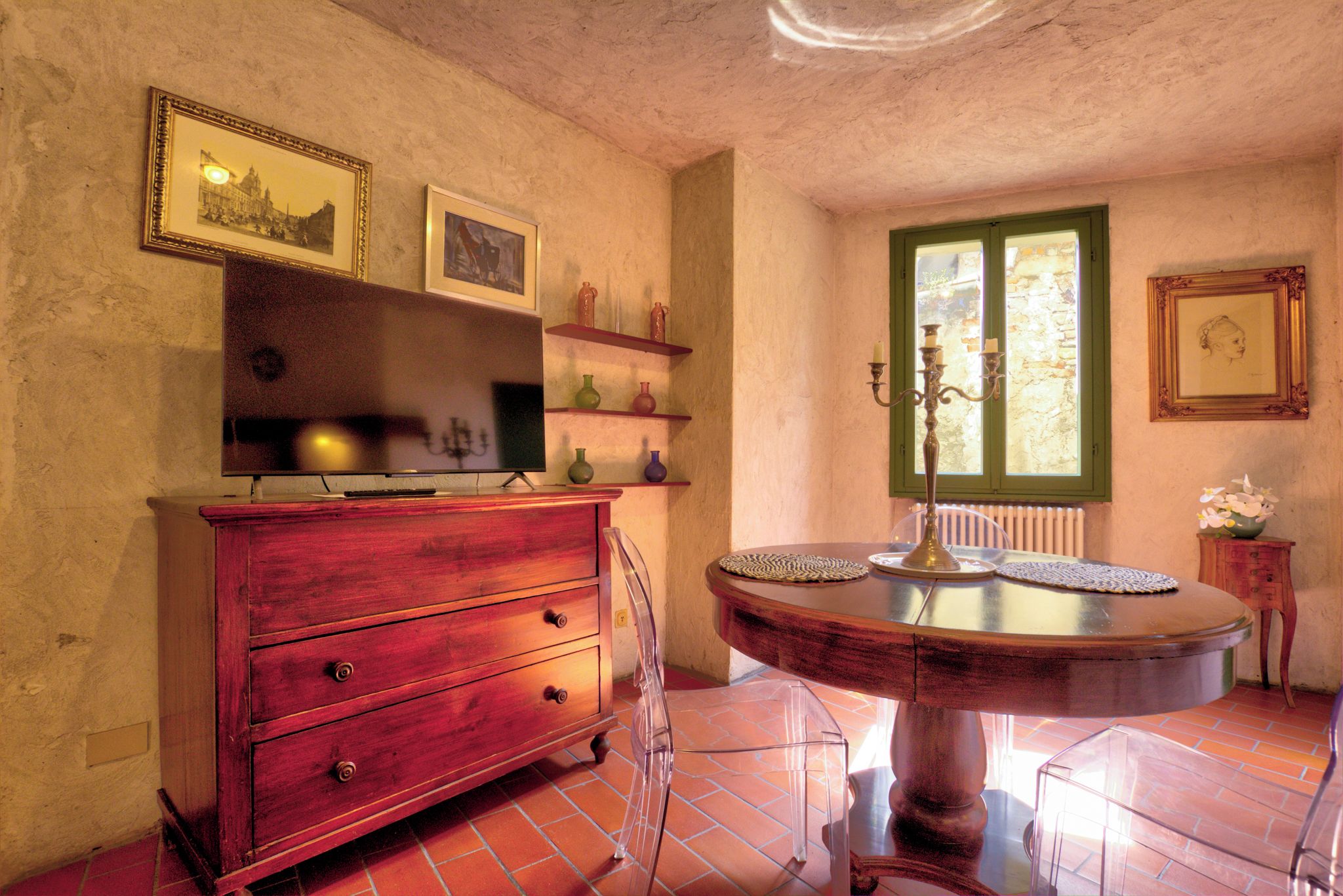 A room with a wooden cabinet, a round table with a glass top, and a window with a view of greenery.