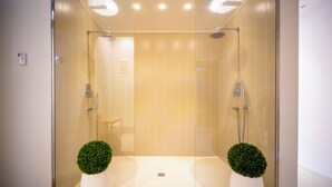 Un área de ducha moderna con puertas de vidrio, piso de baldosas y dos plantas en macetas.