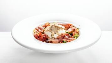 A white plate with a dish of prosciutto, a creamy sauce, and greens.