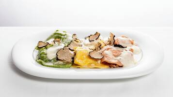 Une assiette blanche contenant divers aliments, notamment des légumes verts, du fromage jaune et de la viande, et peut-être aussi des truffes, le tout présenté sur un fond blanc.