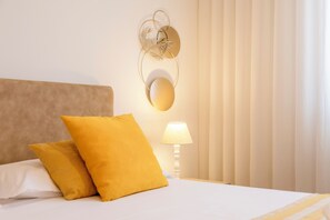 A neatly made bed with white and yellow pillows, a wall-mounted decorative piece, and a bedside lamp.