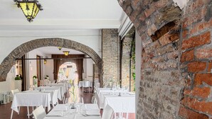 Un restaurante con mesas y sillas blancas, paredes de ladrillo y faroles colgantes.
