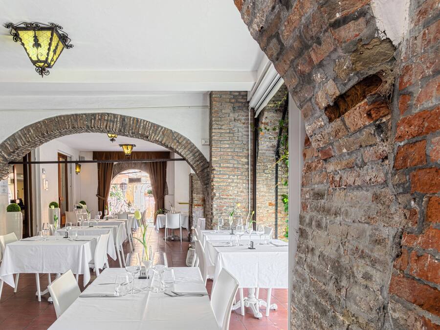 Un ristorante con tavoli e sedie bianche, pareti in mattoni e lanterne appese.