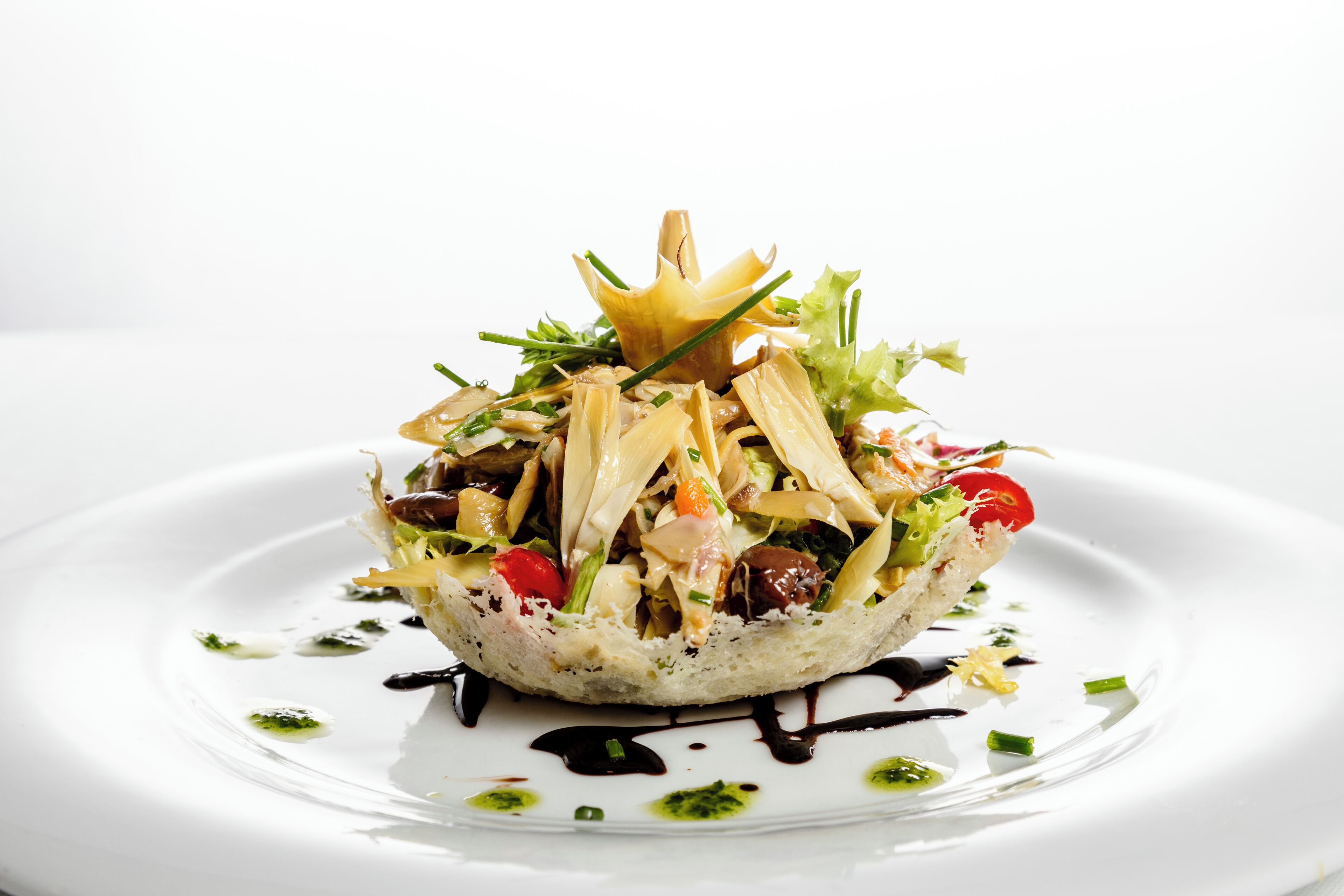 Un piatto bianco con un'insalata sopra una ciotola di pane, guarnito con erbe verdi e condito con salsa.