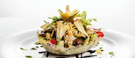 Un plato blanco con ensalada sobre un bol de pan, decorado con hierbas verdes y rociado con salsa.
