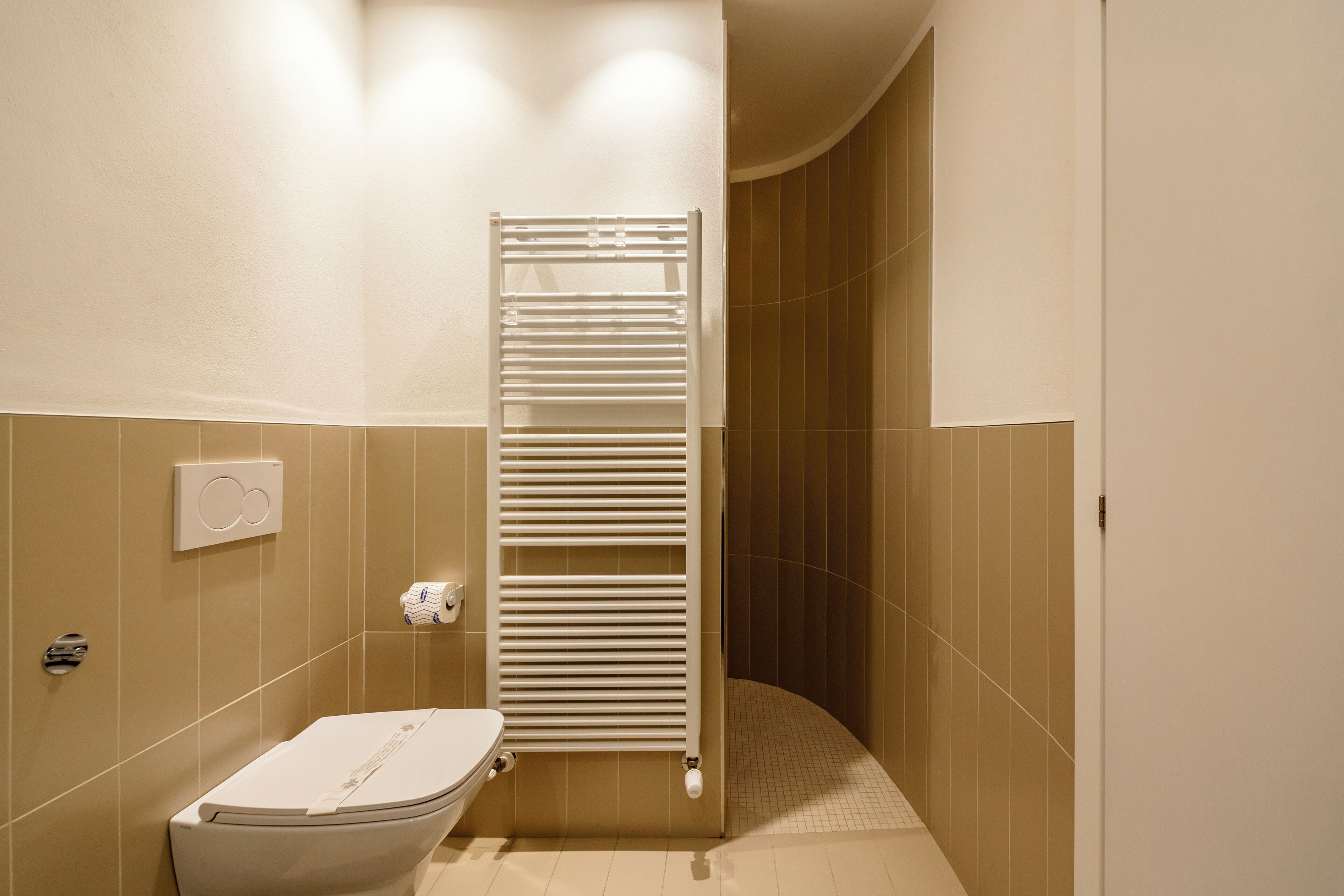 A bathroom with a toilet, a towel rack, and a shower area.
