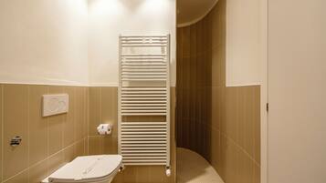 A bathroom with a toilet, a towel rack, and a shower area.