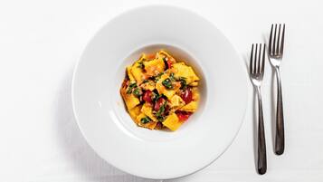 A white plate with a pasta dish and two forks on a white tablecloth.