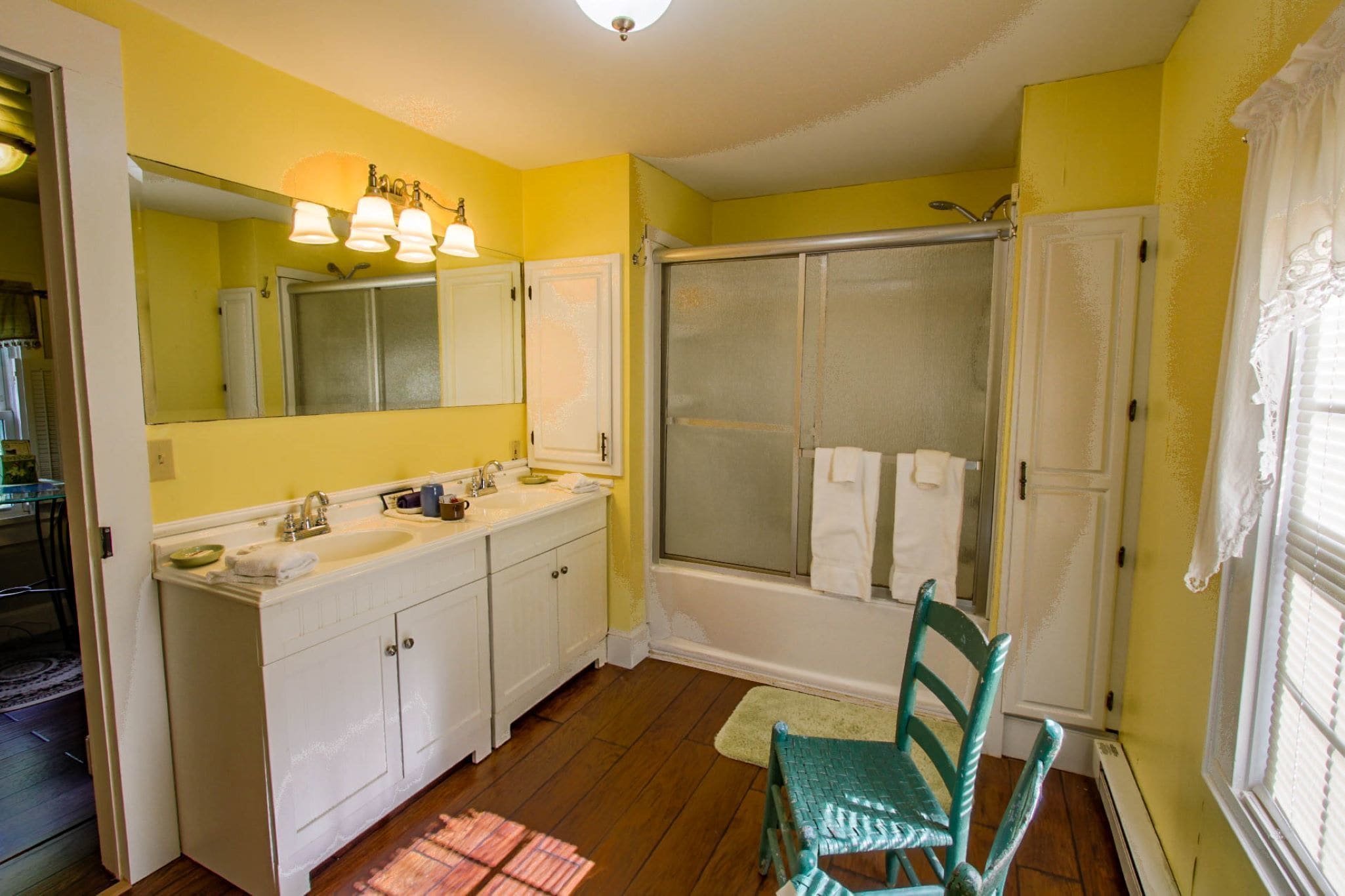 A bathroom with a large mirror, two sinks, a shower, and a chair.