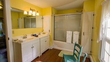 A bathroom with a large mirror, two sinks, a shower, and a chair.