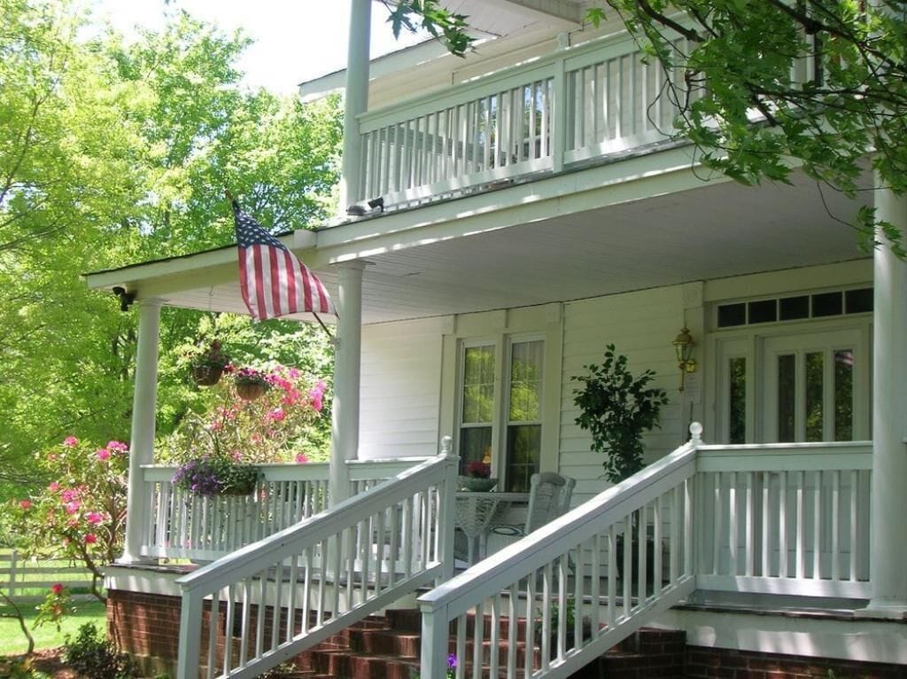 A two-story house with a porch, a flag, and a brick foundation.