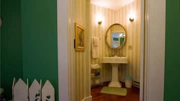 A narrow hallway leading to a bathroom with striped wallpaper, a pedestal sink, and a mirror.