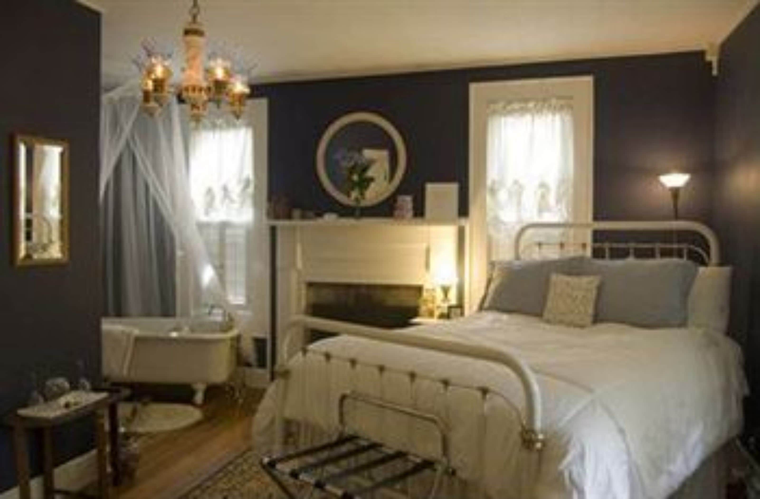 A bedroom with a bed, a bedside table, a mirror, a chandelier, and a window with curtains.