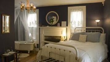 A bedroom with a bed, a bedside table, a mirror, a chandelier, and a window with curtains.