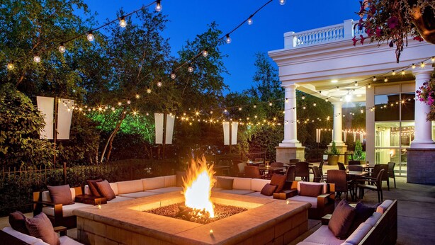 An outdoor seating area with a fire pit, surrounded by sofas and chairs, under string lights. - Hilton Columbus/Polaris (Columbus)