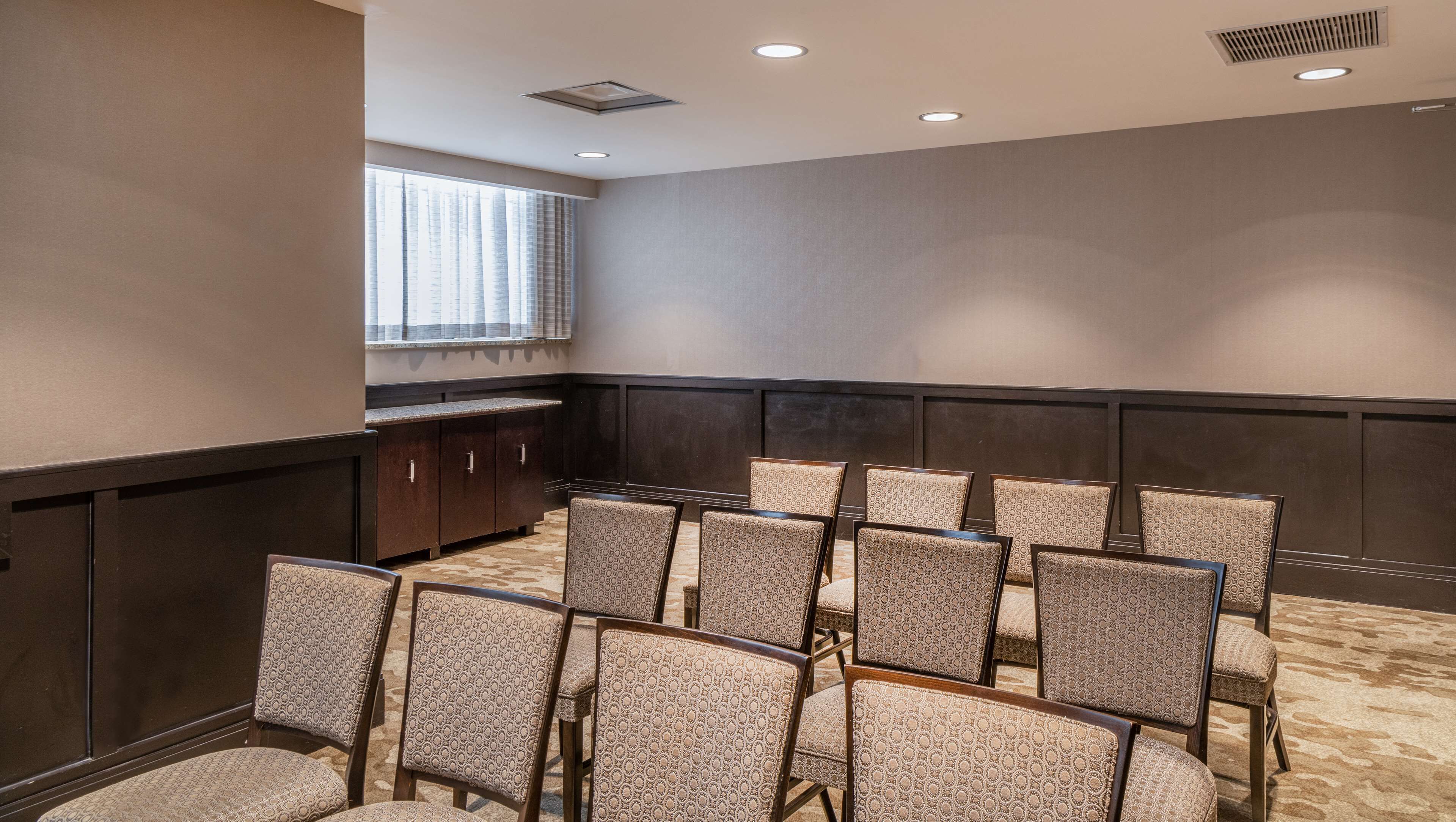 A conference room with a carpeted floor, wooden paneling, and patterned chairs.