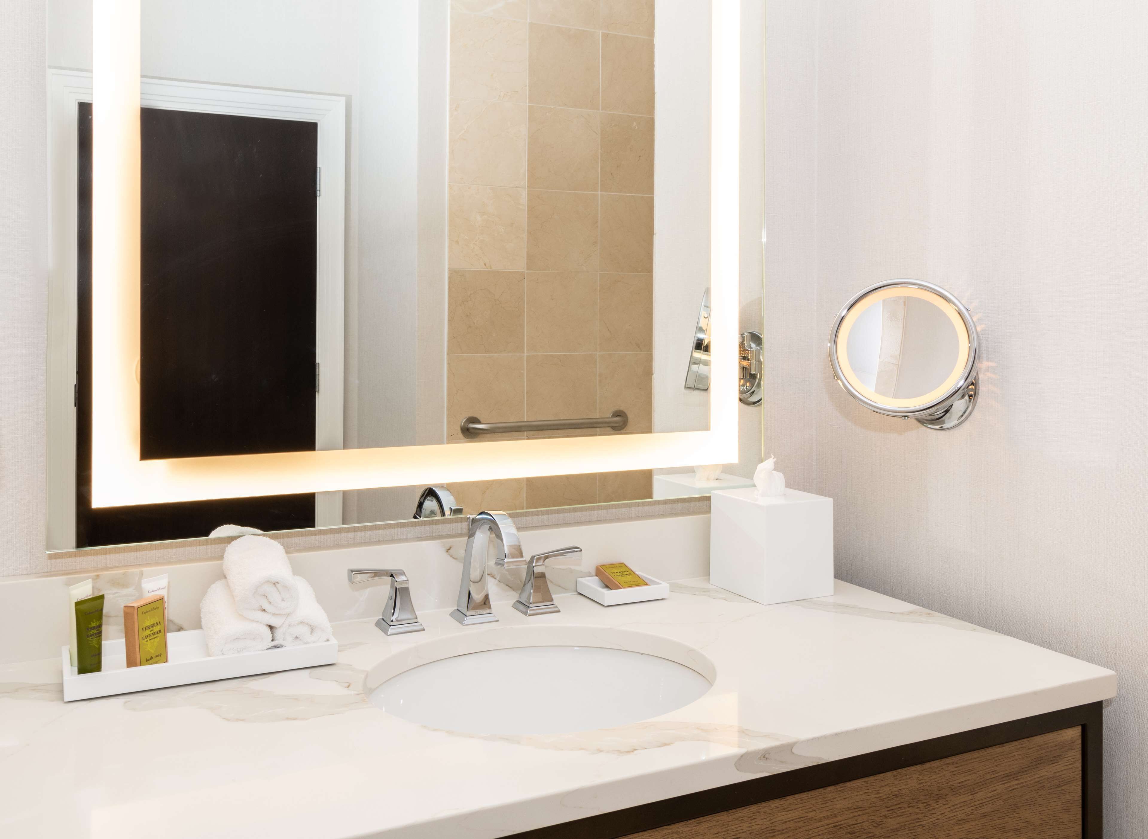 Un baño con lavamanos blanco, un espejo grande y un perchero para toallas.