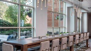 A long dining table with chairs, large windows, and hanging lights. - Hilton Columbus/Polaris (Columbus)