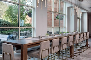 A long dining table with chairs, large windows, and hanging lights. - Hilton Columbus/Polaris (Columbus)